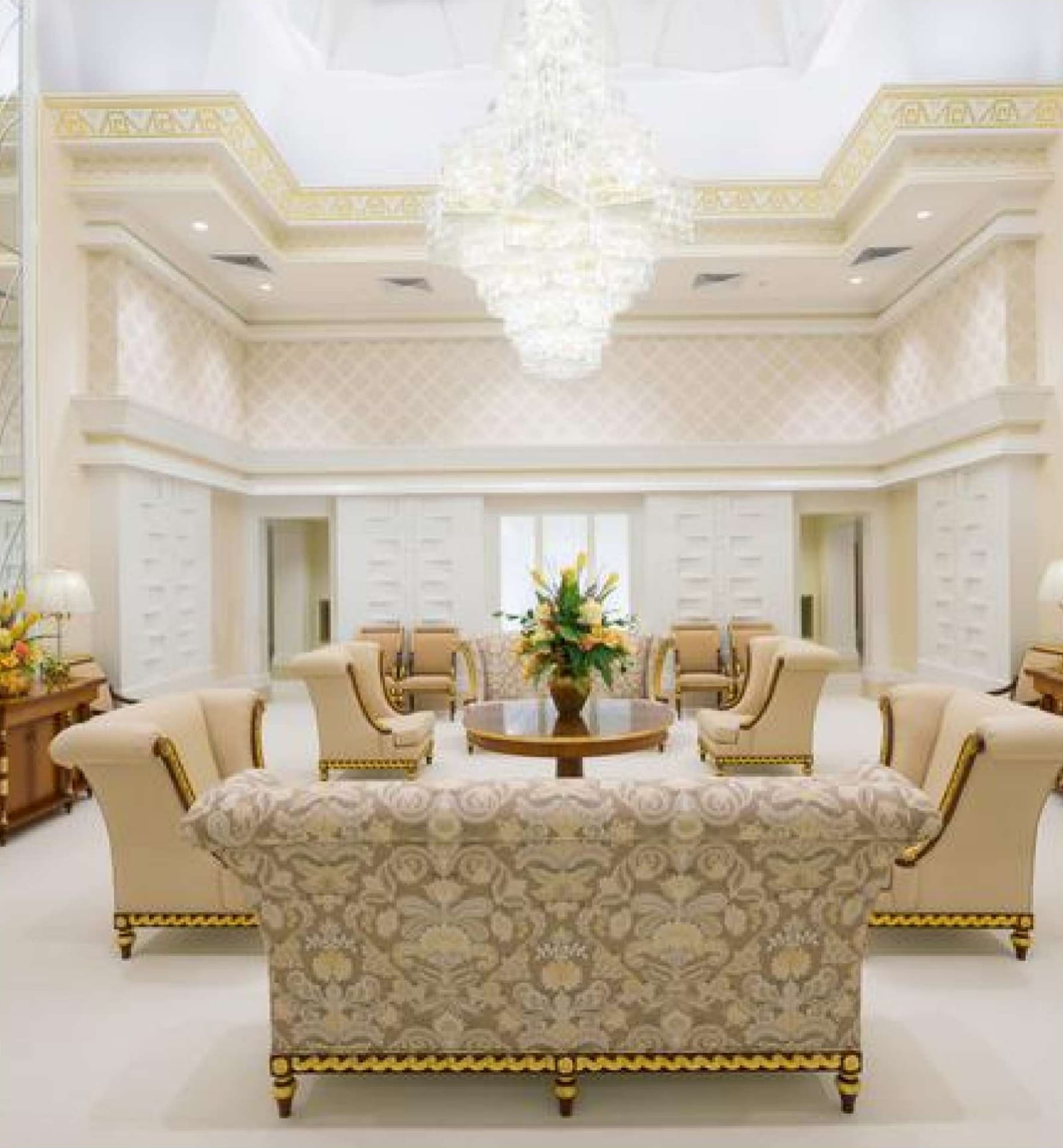 Celestial room: a bright white and gold room with a crystal chandelier, upholstered armchairs, and a sofa arranged around a table with flowers