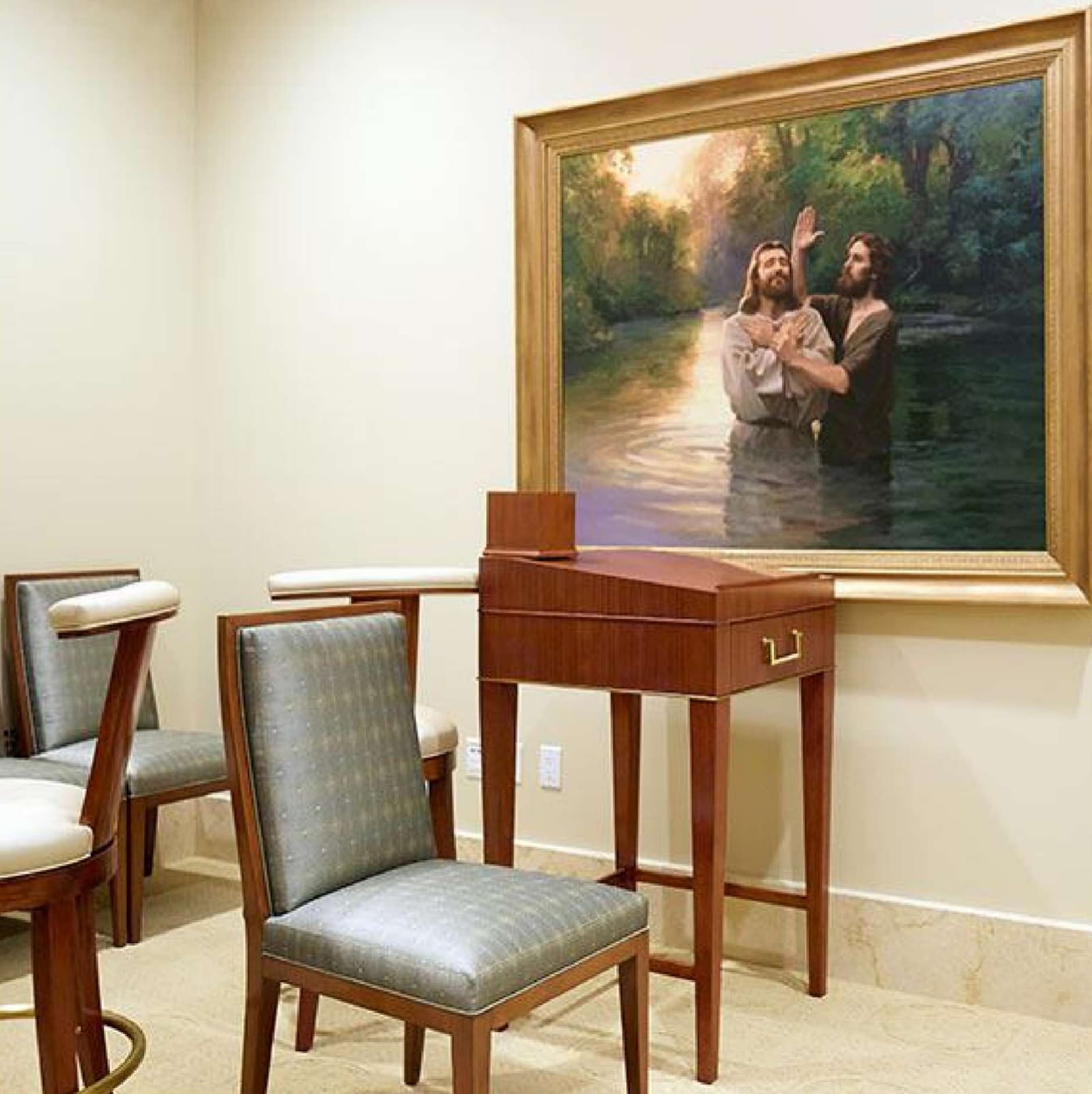 Confirmation room: upholstered chairs beside a small wooden desk, beneath a framed painting of the baptism of Jesus