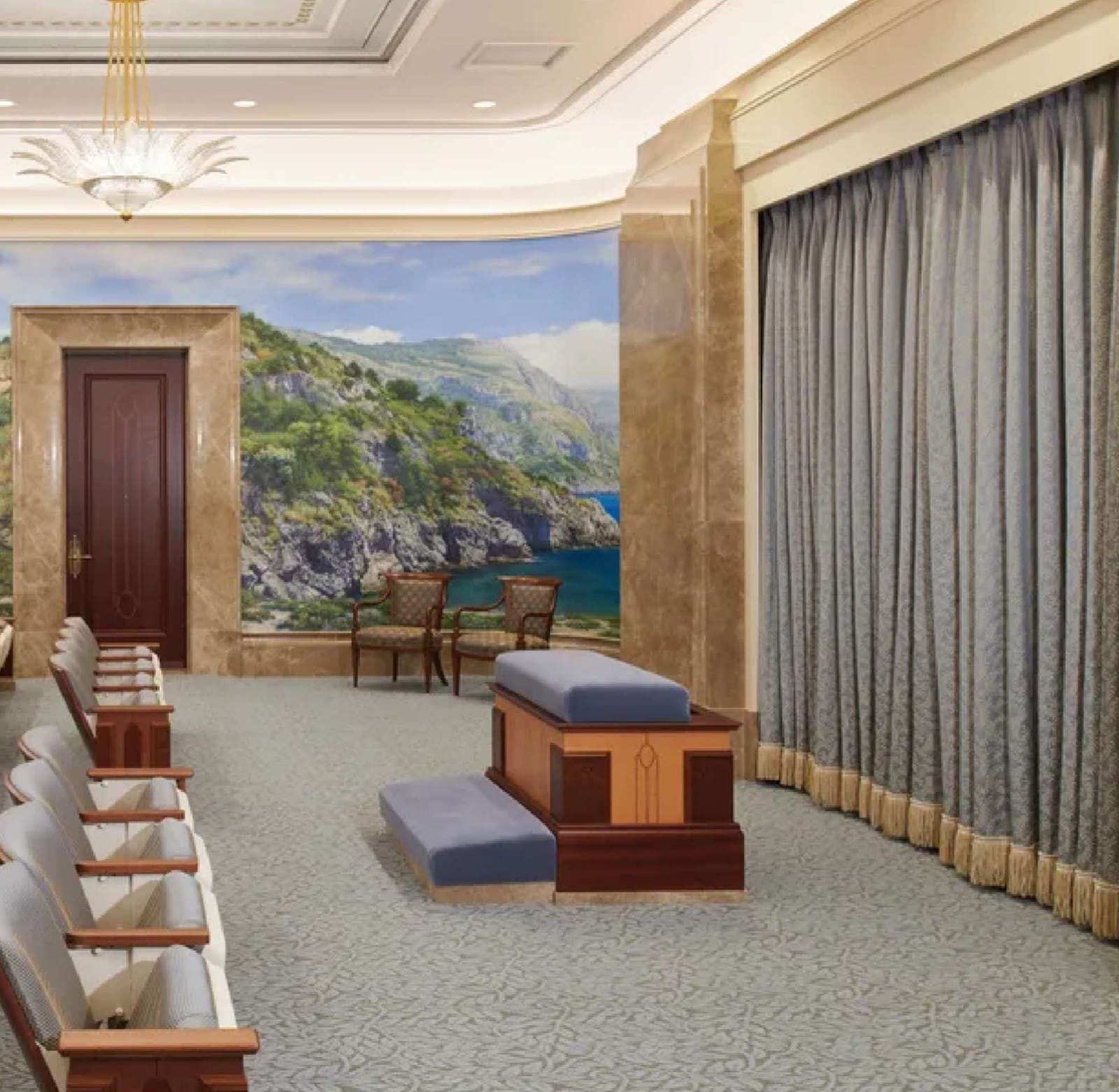 Instruction room: rows of upholstered seats facing a large coastal landscape mural and a curtained wall, with an altar at the center