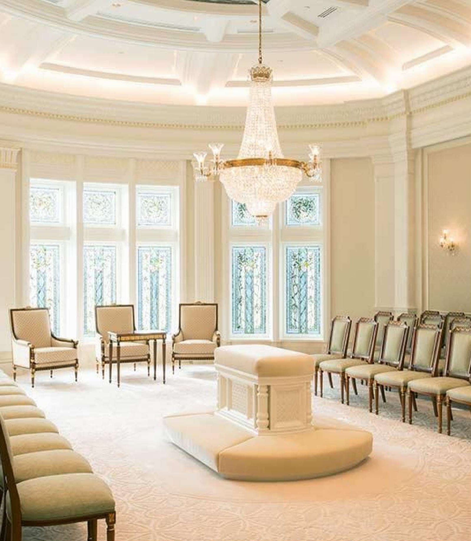 Sealing room: a white altar at the center of a bright room with a crystal chandelier, stained-glass windows, and chairs along the walls
